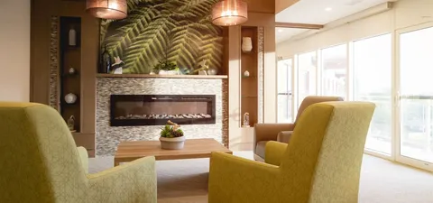 Room with two green armchairs, a small table and a fireplace