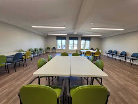 Activity room with tables, green chairs and large windows.