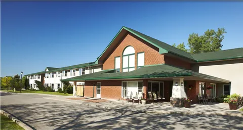 Brick and sided building with green roofs, a covered entrance and patio chairs