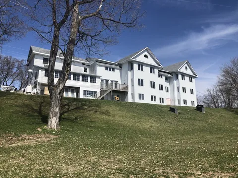Three-storey white residence on a grassy slope behind bare trees