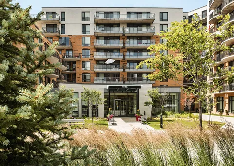 Residence facade and glass entrance beyond planted beds and trees