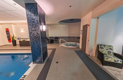 Indoor swimming pool and whirlpool with handrails and chairs beside windows