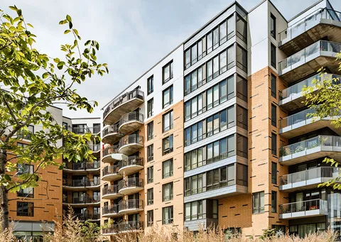Brick residence building with balconies beside trees and landscaped borders