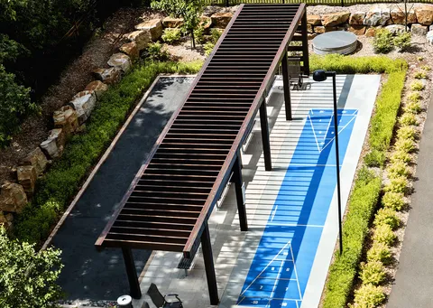 Outdoor shuffleboard court and pergola beside garden paths and planted beds