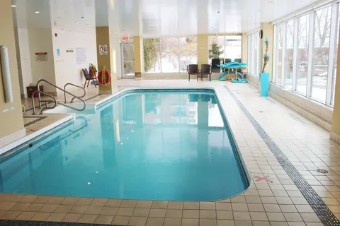 Indoor swimming pool with a tiled deck and large windows.