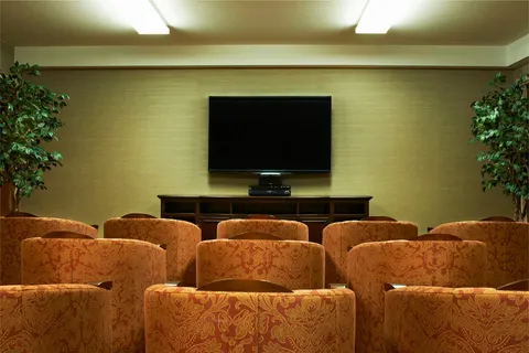Room with rows of upholstered seats facing a television