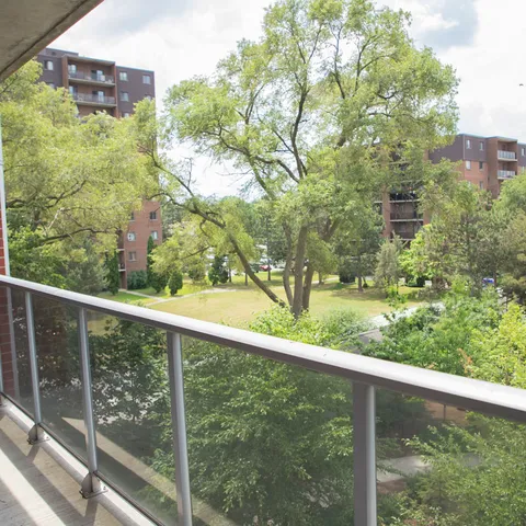 Glass balcony railing overlooking trees, lawn and neighbouring buildings