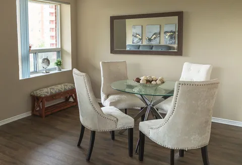 Glass table with four upholstered chairs beside a window and large wall mirror