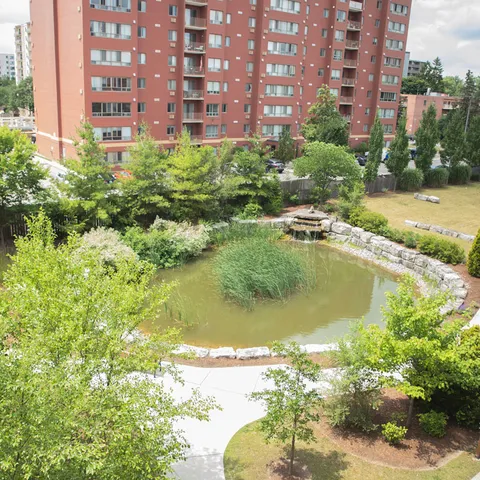Red brick residence beside a landscaped pond, trees and paved garden paths