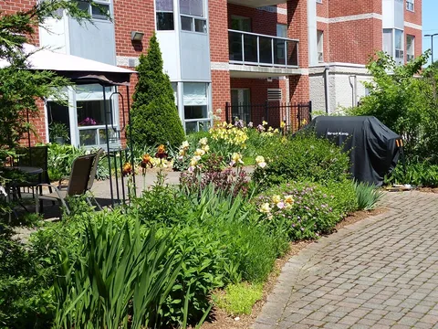 Flower beds beside a brick path, patio chairs and a covered barbecue