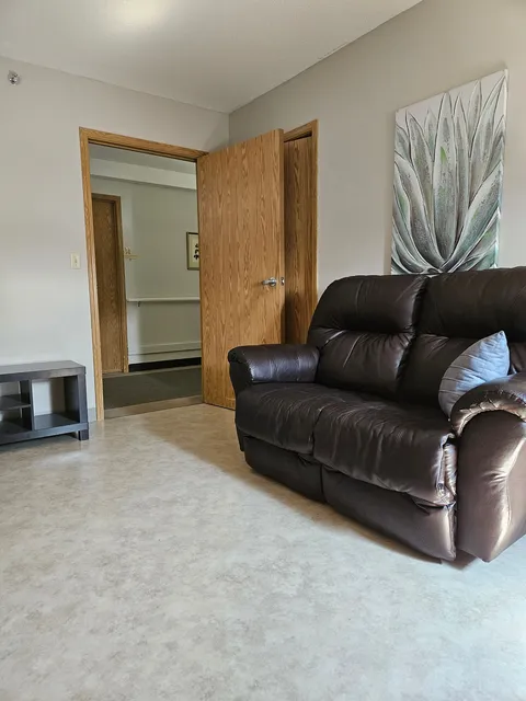 Suite sitting area with a leather sofa, leaf artwork and an open doorway.