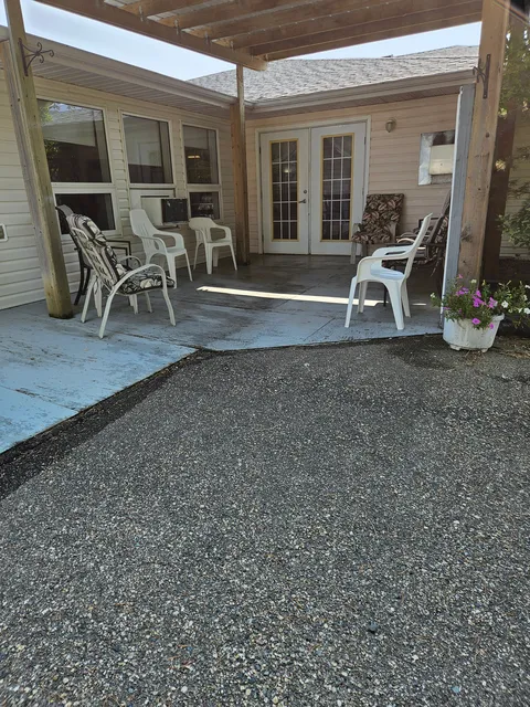 Covered patio with outdoor chairs and potted flowers beside glazed doors.