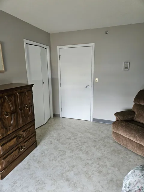 Bedroom with a wooden dresser, an armchair and white closet doors.