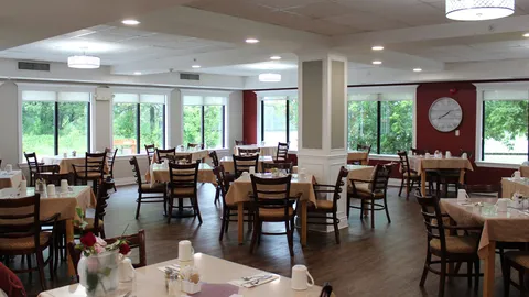 Dining room with cloth-covered tables, wooden chairs and large windows