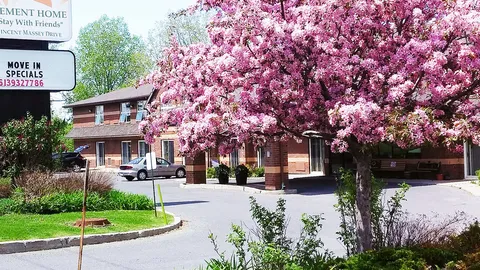 Brick residence behind a flowering pink tree, with a covered entrance and driveway