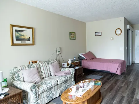 Room with a pink-covered bed, floral sofa, wooden coffee table and framed landscape pictures