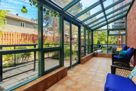 Glass-roofed sunroom with wicker chairs and blue cushions