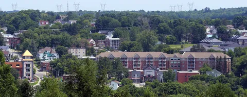 Elevated view of a red-brick residence with balconies among trees and surrounding houses.