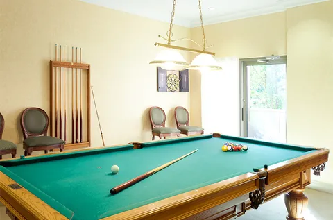 Room with a green pool table, chairs and a dartboard