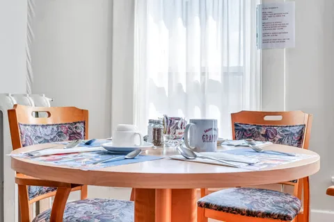Round dining table set with cups and cutlery beside a curtained window