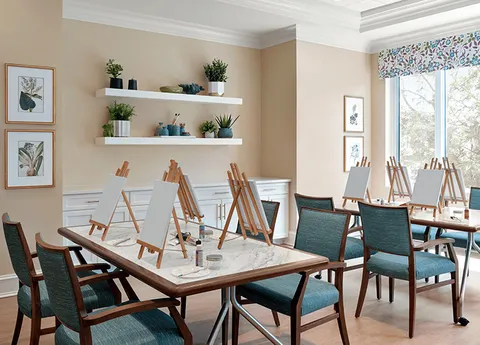 Art room with tables, chairs, small easels and plant shelves.