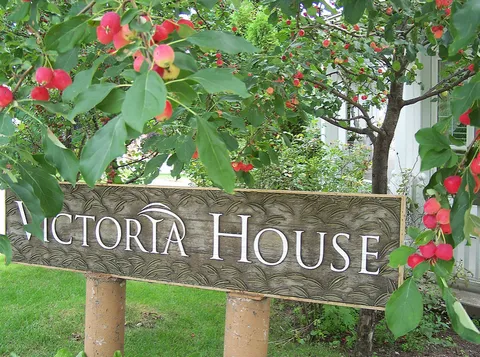 Wooden Victoria House sign beneath leafy branches