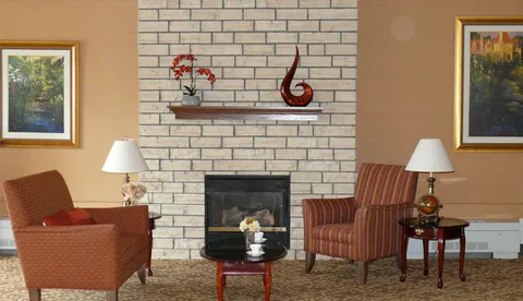 Two armchairs beside a white brick fireplace and framed landscape pictures