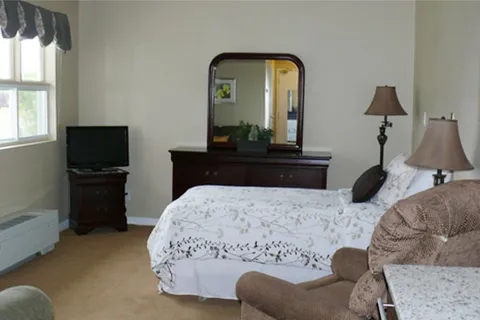 Bedroom with a bed, upholstered armchair, dresser and television