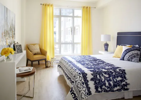 Bedroom with blue patterned bedding, an armchair and yellow curtains