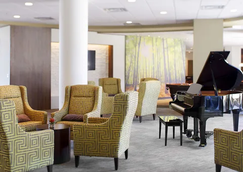 Grand piano and patterned armchairs beside windows and a woodland mural
