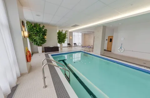 Indoor swimming pool with handrails, plants and chairs