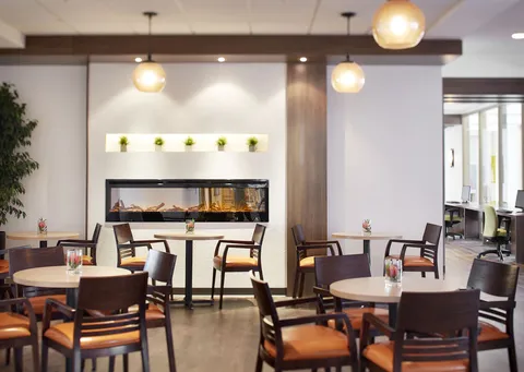 Round cafe tables and wooden chairs beside a long fireplace