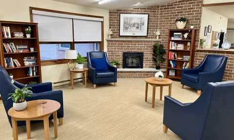 Library lounge with armchairs, bookshelves and a brick fireplace.