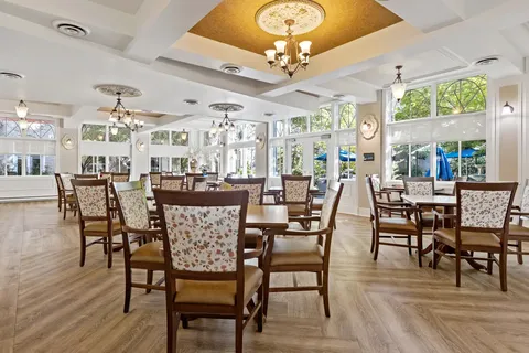 Dining room with wooden chairs, round tables, chandeliers and broad windows
