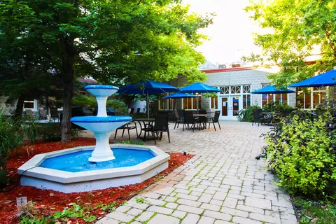 Paved courtyard with a blue fountain, tables, umbrellas and a glass-walled room
