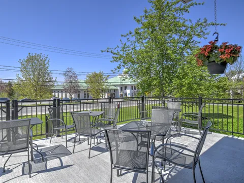Outdoor terrace with metal tables and chairs beside a lawn and trees.