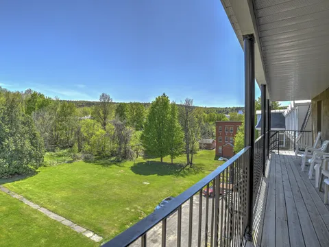 Covered wooden balcony with white chairs overlooking a lawn and trees.