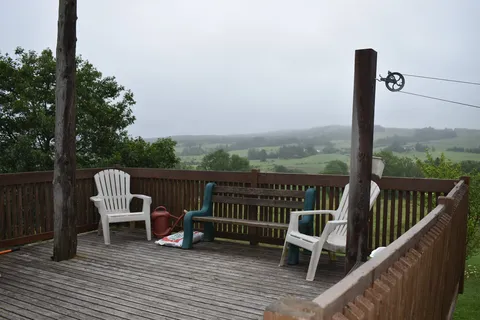 Raised wooden deck with chairs overlooking rural fields.