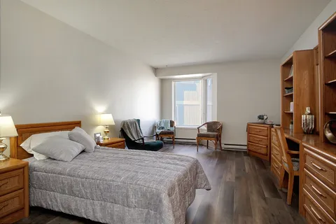 Suite bedroom with a bed, armchairs, wooden storage and a balcony door.