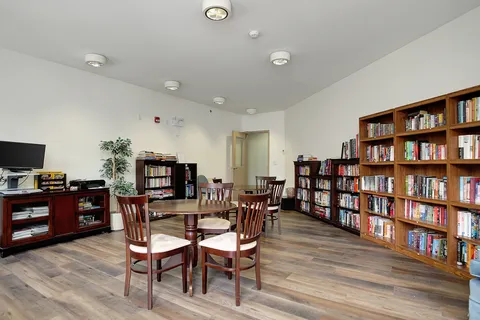 Library with bookcases, tables, chairs and a television.