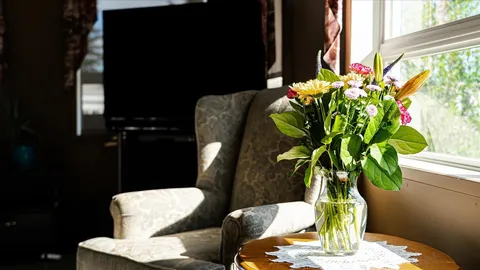 Armchair beside a table with a vase of flowers, a window and a television
