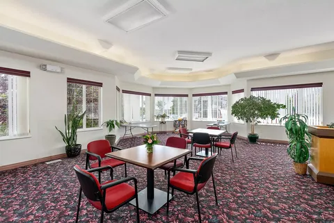 Room with red chairs and square tables beside large windows
