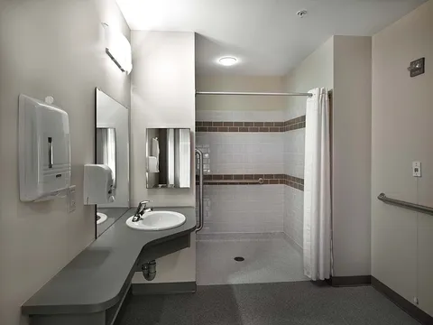 Bathroom with a sink, open shower, mirrors and support rails