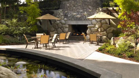 Patio with tables, chairs, umbrellas, a stone fireplace and a pond.