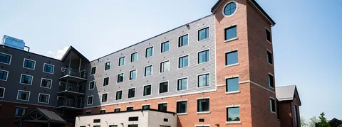 Multistorey building with grey siding, brick walls, balconies and a pitched entrance roof