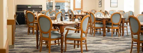 Dining tables and upholstered chairs beside large windows and landscape pictures