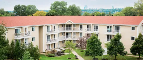 Residence building with a red roof, balconies, trees and a front garden.