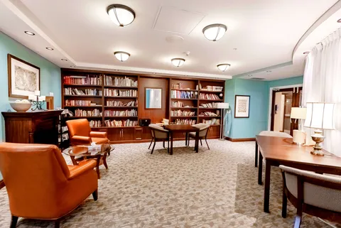 Armchairs and a table in a room lined with wooden bookshelves