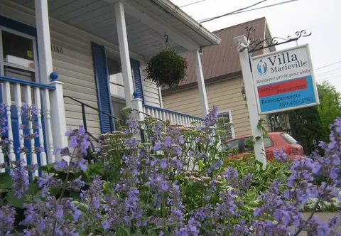 Front porch with blue railings, purple flowers and a Villa Marieville sign