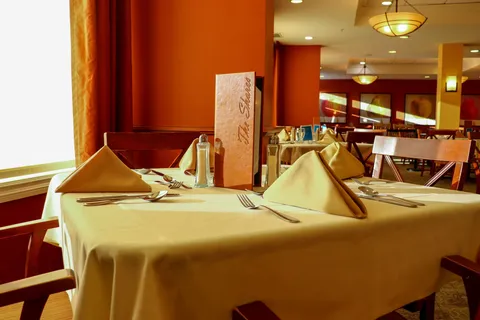 Dining table with a menu, folded yellow napkins and cutlery beside a window